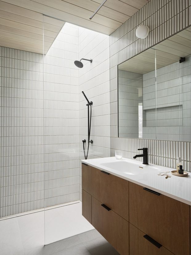 Contemporary bathroom with a walk-in tiled shower, white vertical-ridged wall tiles, pale timber-look ceiling panels, a large mirrored vanity wall, and a floating wood vanity with a white integrated basin and matte black tapware. The space is bright, clean, and minimally styled.