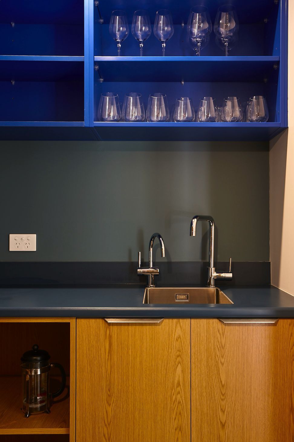 The scullery combines practical storage with bold material choices. A grey Formica benchtop is paired with oak cabinetry below and cobalt blue Melteca overhead cupboards, creating a functional yet beautifully detailed workspace.