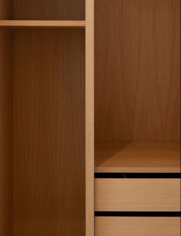 Close-up detail of built-in timber joinery, showing warm medium-brown wood-grain cabinetry with open shelving and lighter wood drawer fronts separated by dark recessed gaps. The image focuses on the material, grain, and precise vertical and horizontal lines of the fitted storage.