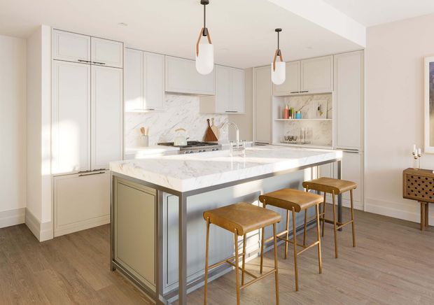 Bright, refined kitchen with a large central island featuring a white marble-look benchtop, integrated sink and seating for four. The room has full-height pale grey cabinetry, an open display shelf, warm timber-look flooring, and three pendant lights with white glass shades and dark metal details. A small timber console is visible at the right edge.