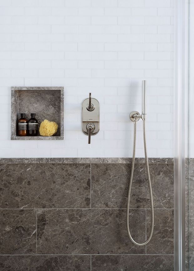 Close-up view of a contemporary shower enclosure featuring white subway wall tiles, dark grey veined stone wall tiles, a recessed stone-lined niche with toiletries, and polished chrome shower controls and handheld shower rail. A glass shower screen is visible at the right edge.
