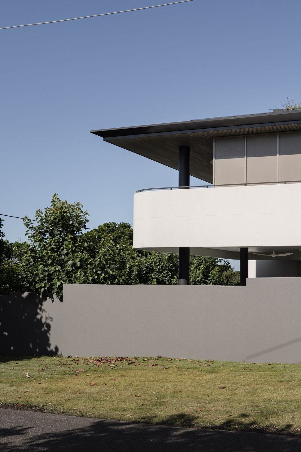 Decade House - Exterior. Upper level with a fine edged roof and white balcony above a rendered garden wall.