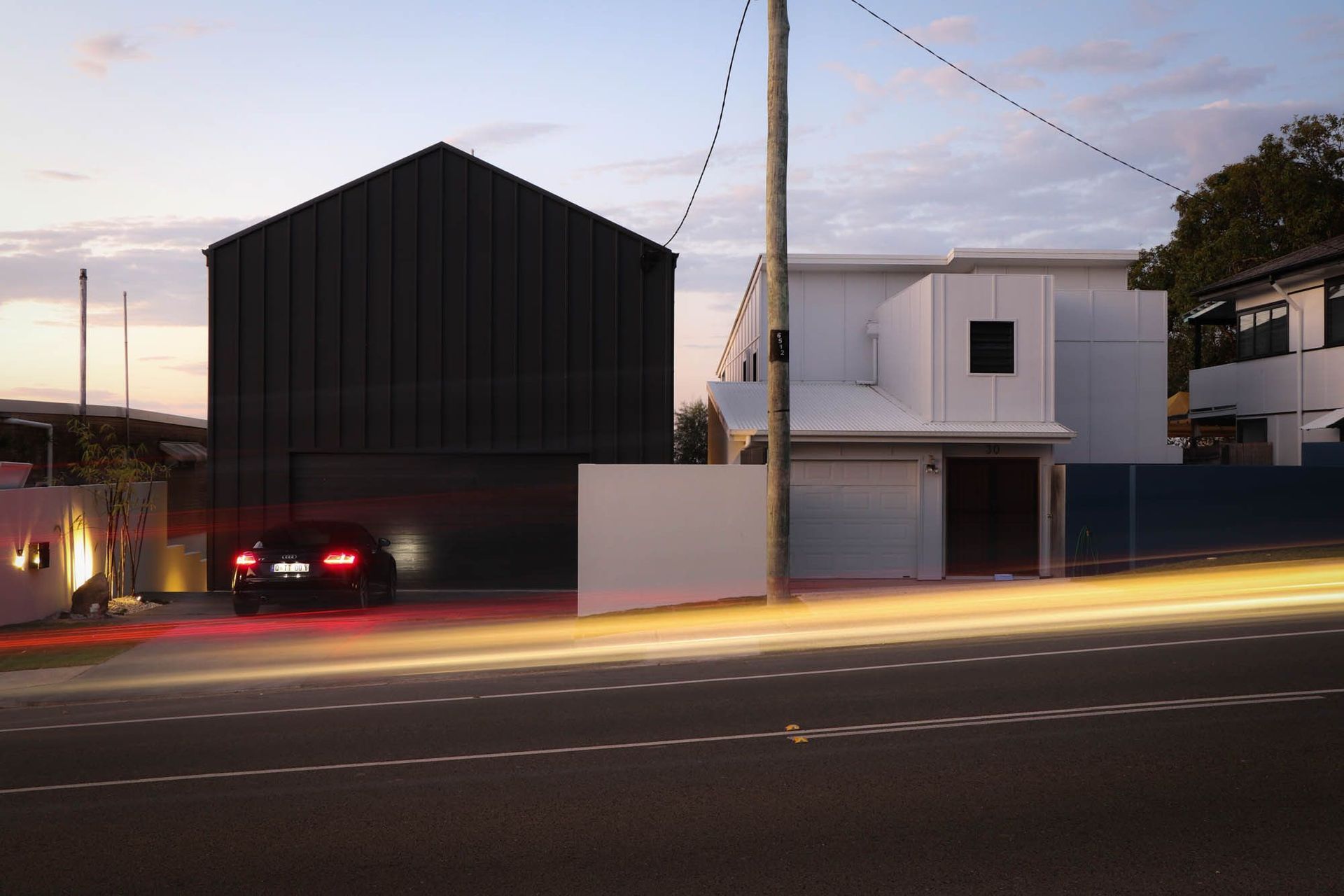 Anderson Residence - Exterior. Street view at dusk with light trails past the dark gabled home.