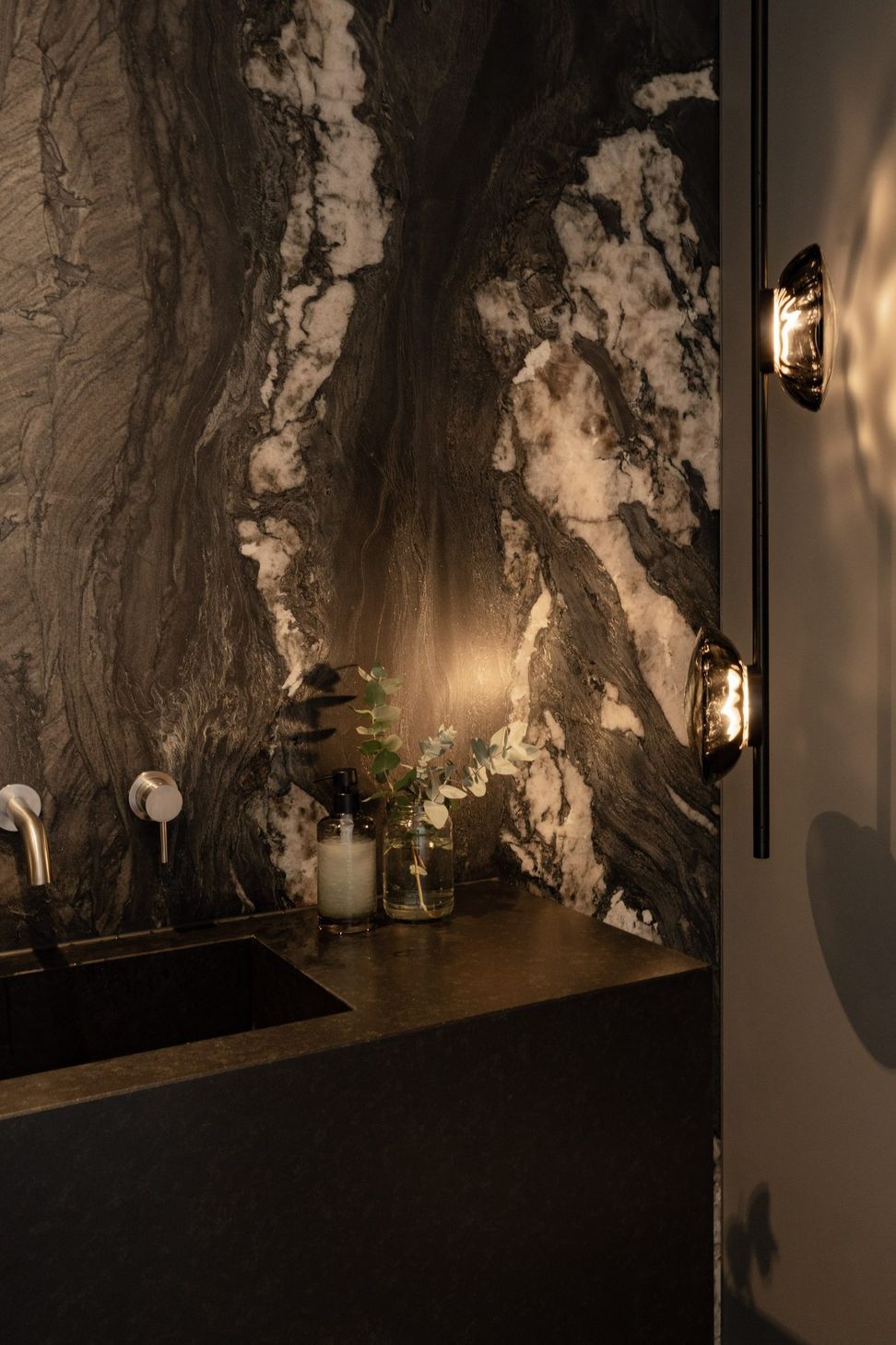 Decade House - Powder Room. Powder room with a dramatic veined stone feature wall and warm wall sconces.