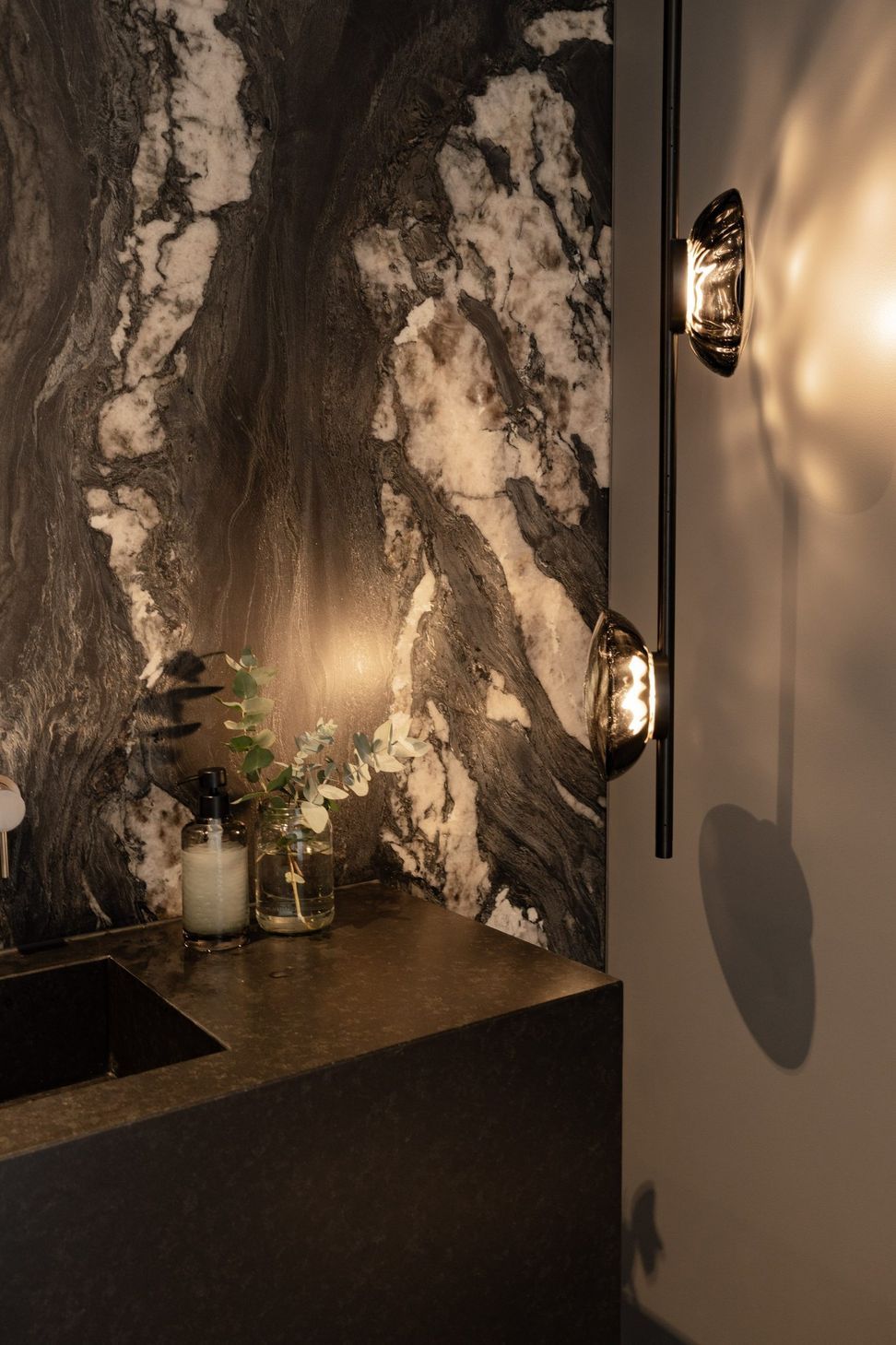 Decade House - Powder Room. Close view of the veined stone wall and sconce lighting.