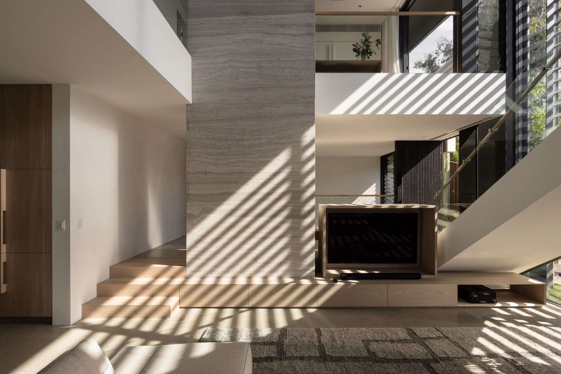 Decade House - Living Room. Double height living space with a travertine fireplace wall and sunlight through the louvres.