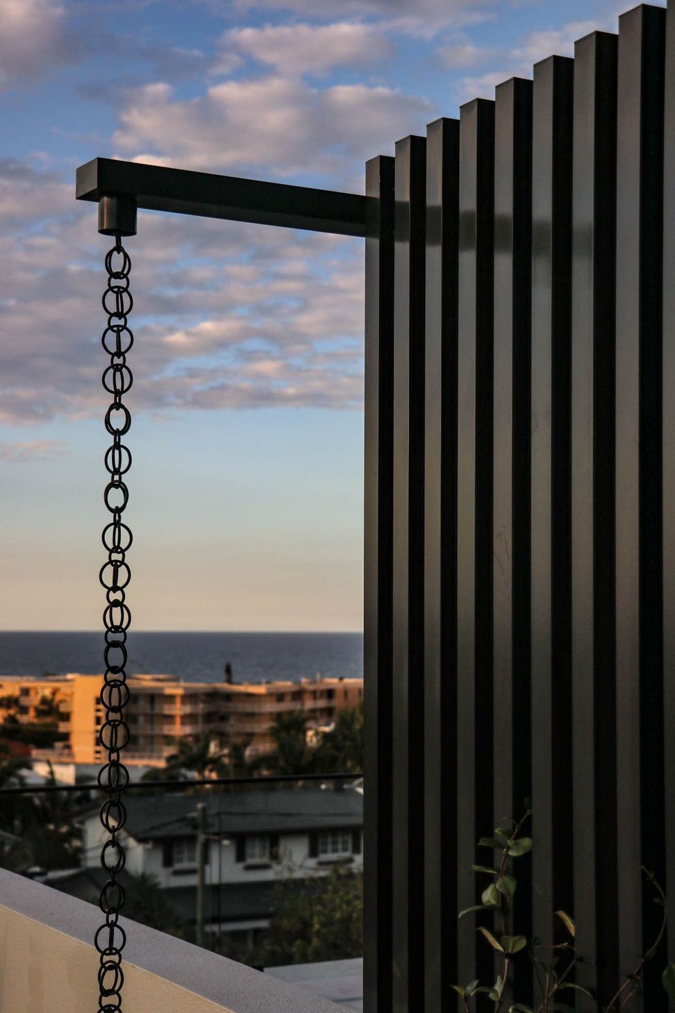 Anderson Residence - Balcony. Rain chain against dark cladding and the coastline.