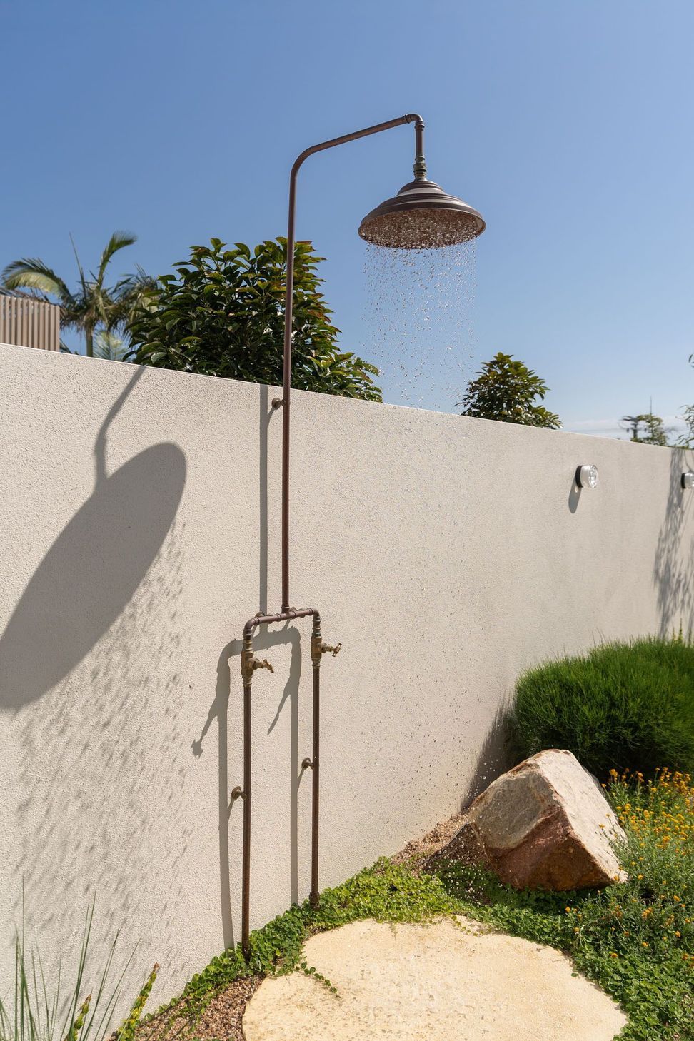 House on Pacific - Exterior. Outdoor shower against a white rendered wall with native planting.