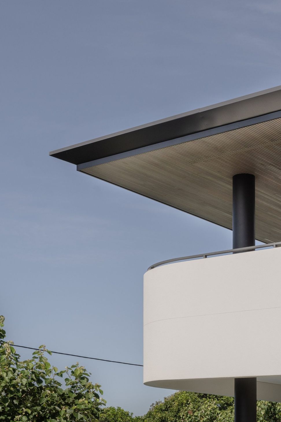 Decade House - Exterior. Fine roof edge and curved white balcony against the sky.
