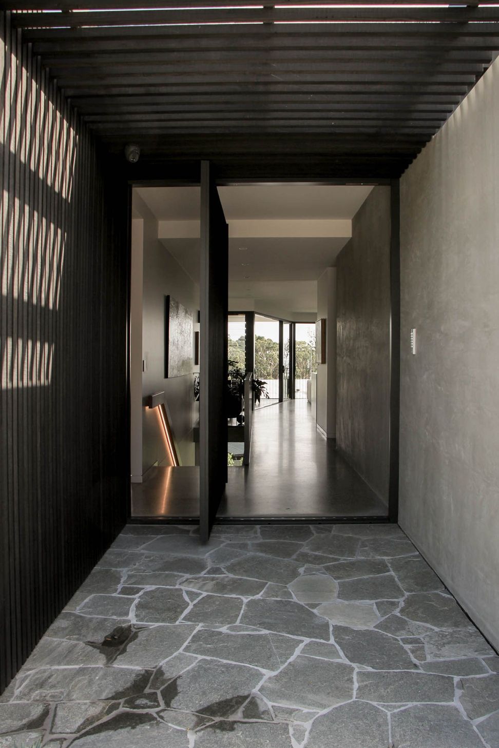 The Dual House - Entry. Pivot door opening to a long concrete hallway.