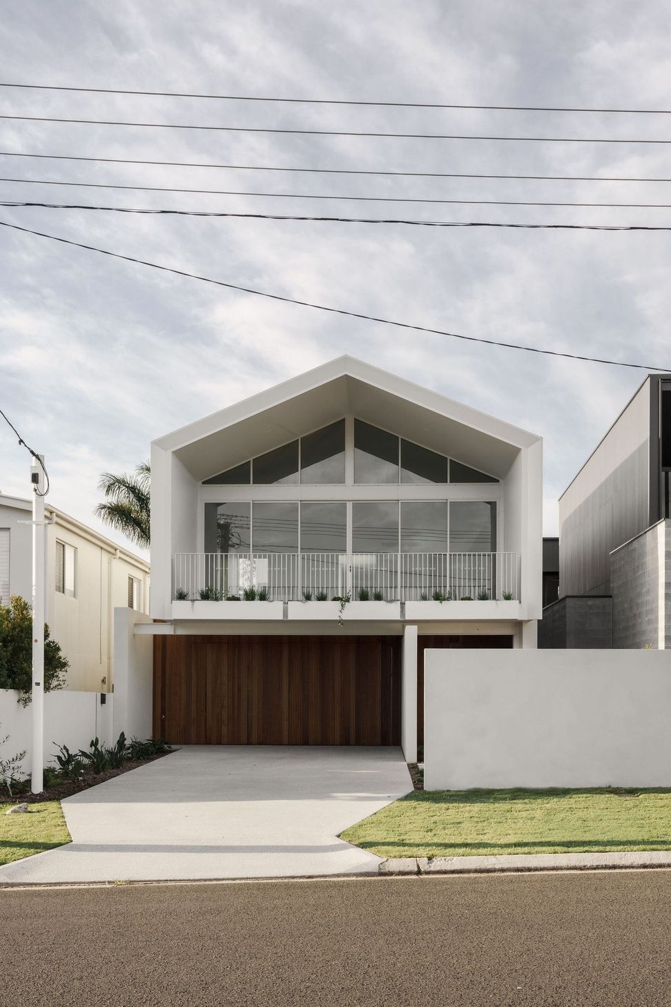 Gilbert Residence - Exterior. Gabled facade with a glazed balcony above timber garage doors.