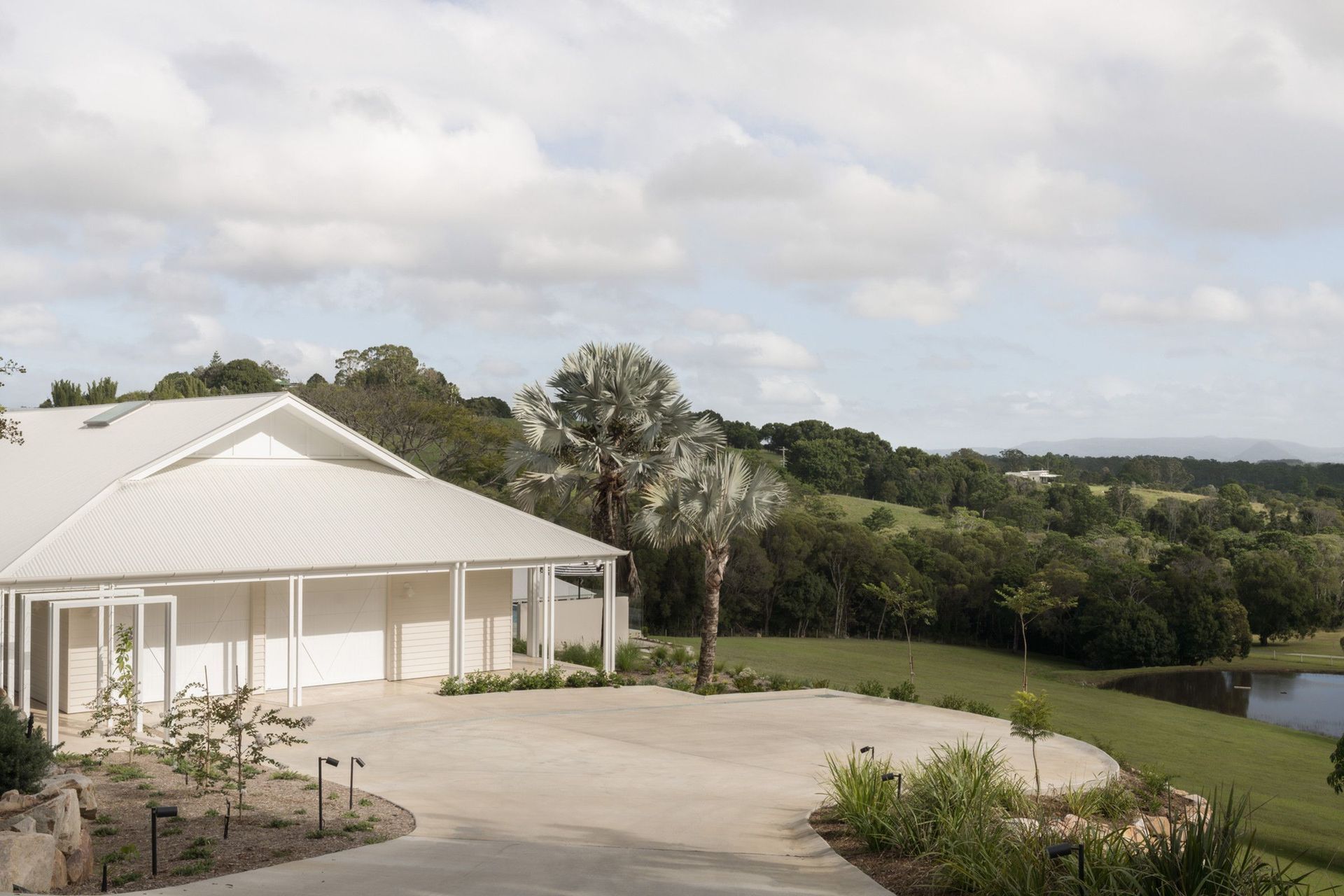 Euroa Farm - Exterior. The farmhouse set on rolling lawn beneath palms.