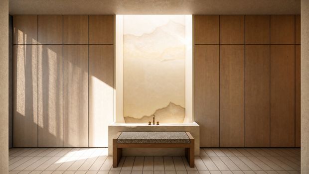 Warm, minimalist interior with full-height dark timber wall panelling, a central stone or plaster vanity with integrated basin, a softly illuminated organic feature panel above it, and a simple timber bench. Large square floor tiles and strong sunlight create a calm, refined atmosphere.