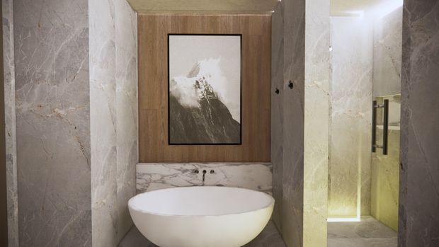 A refined bathroom featuring a freestanding oval bathtub against a warm wood-panelled wall, with a marble vanity backsplash, large marble-clad walls, framed monochrome artwork, and a glass-enclosed shower with dark metal hardware.