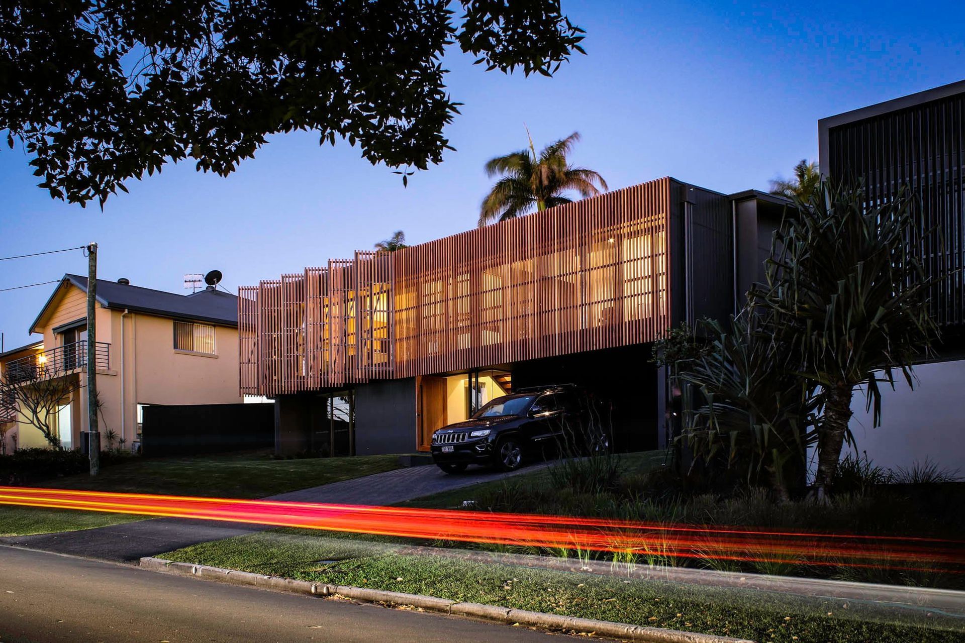 Glennon Residence - Exterior. Battened upper level glowing above the street at dusk.