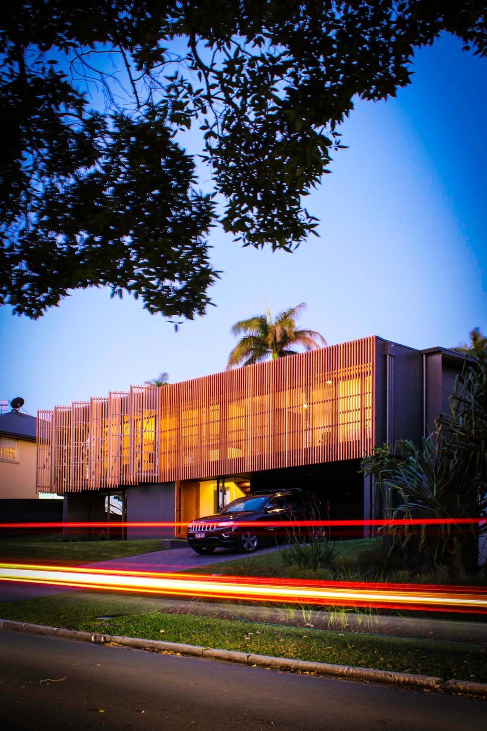 Glennon Residence - Exterior. Timber screens glowing at sunset beneath a palm.