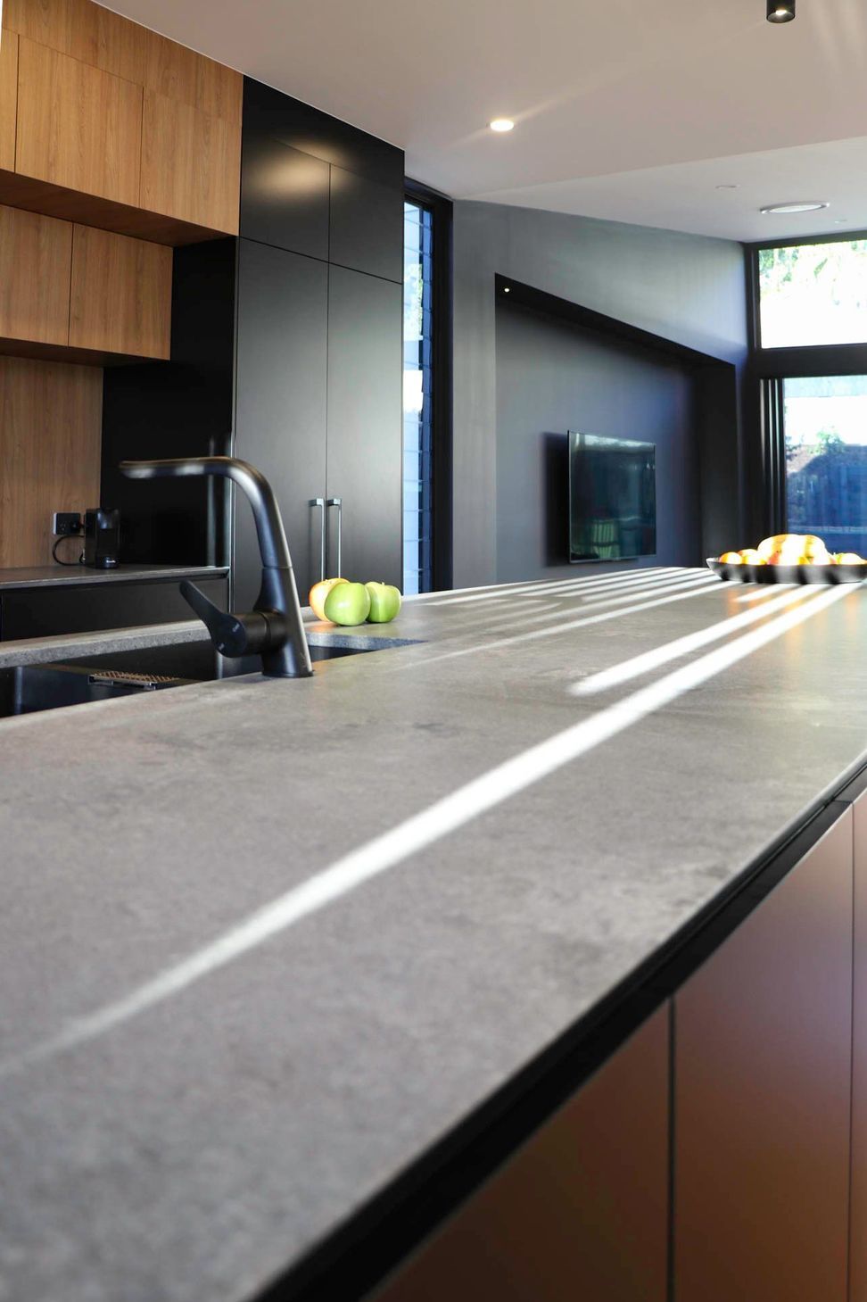 Glennon Residence - Kitchen. Concrete benchtop and dark tapware in the light.