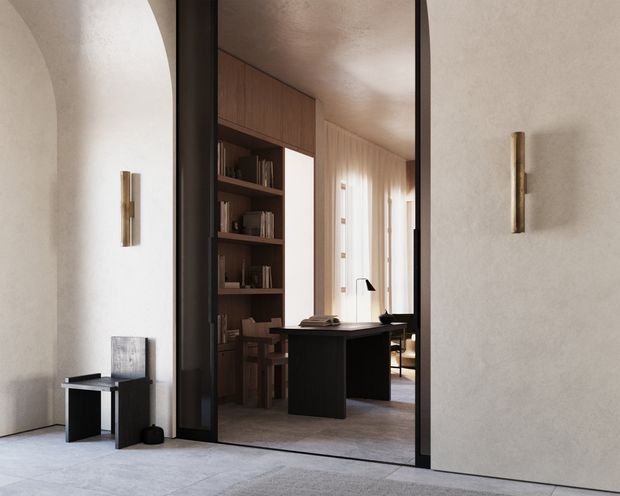 A refined interior view through a tall black-framed opening into a compact home office or study. The foreground has softly textured light plaster walls, a minimalist side table, and slim wall sconces. Beyond the opening is a warm timber built-in bookcase and cabinetry, a dark central desk, sheer curtains, and a calm neutral palette. The space feels understated, warm, and contemporary, with a high-quality minimalist fit-out.
