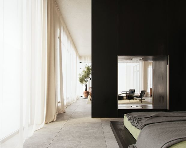 A bright, refined bedroom with floor-to-ceiling sheer curtains along one side, large pale stone or concrete-look floor tiles, and a dramatic black feature wall containing a mirrored opening. The foreground shows a neatly made bed with dark grey bedding and a substantial dark platform base. The mirror reflects a minimalist seating area, reinforcing the open, contemporary interior. The palette is predominantly white, light grey, charcoal and dark wood tones.