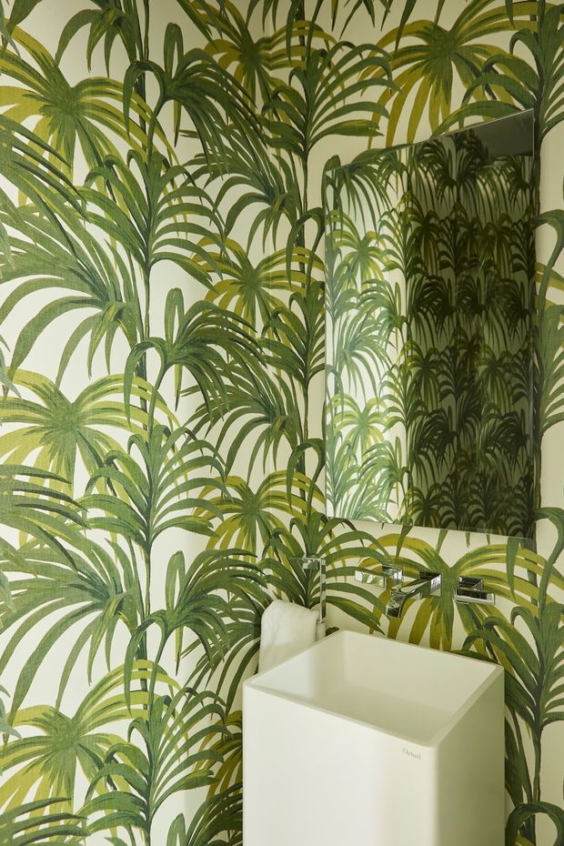 A compact bathroom featuring a white square vessel basin with wall-mounted chrome tapware, a large rectangular mirror, and bold green tropical palm-patterned wall covering throughout. The space has a bright, playful botanical character with high visual contrast between the patterned walls and white sanitaryware.