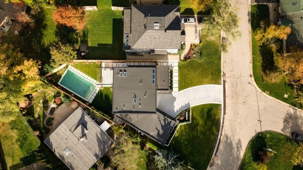Aerial top-down view of a suburban residential property, showing several pitched- and flat-roofed homes, landscaped gardens, a rectangular swimming pool, paved paths, driveways, and a residential street.