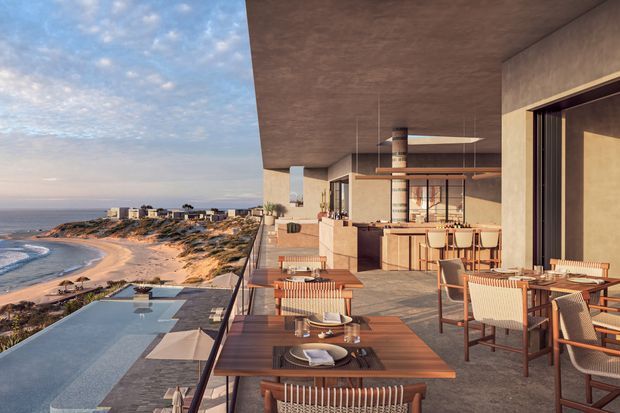 A contemporary coastal outdoor dining and entertaining terrace overlooking a sandy beach and ocean. The expansive covered terrace includes timber dining tables, woven chairs, a built-in outdoor kitchen or bar, pendant lighting, glass balustrades, and an infinity-edge pool below. Warm earthy finishes and floor-to-ceiling glazing create a refined resort-like atmosphere.
