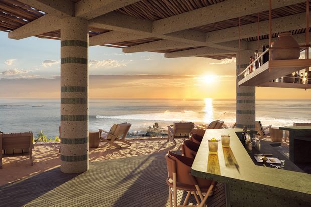 Open-air coastal terrace overlooking the ocean at sunset, with substantial textured concrete columns, exposed timber roof slats, a raised mezzanine or balcony, timber decking, outdoor lounge seating, and a stone or concrete bar counter with stools.