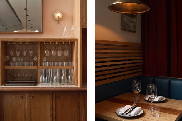 A warm, richly detailed dining and entertaining interior featuring built-in timber glassware cabinetry, a mirrored upper section, decorative wall lighting, and a banquette dining nook. The dining table is set with plates, cutlery, wine glasses, and a dark upholstered bench. Timber slatted wall detailing and deep burgundy wall panels create a refined, intimate atmosphere.