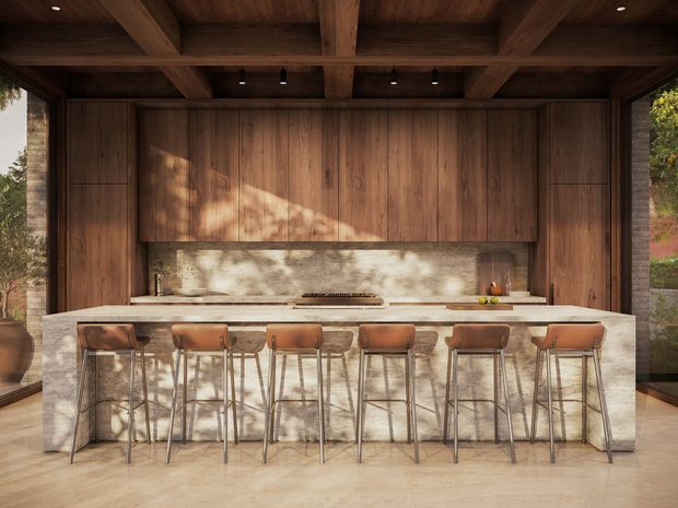 A large, refined kitchen with a long stone island and seating for six or more. Warm dark timber cabinetry and a coffered timber ceiling frame the space, while a full-height pale stone splashback and matching island create a natural, earthy contrast. Floor-to-ceiling glazing at both sides brings in views of surrounding greenery and ample daylight. Slim pendant and recessed lighting, integrated appliances, and leather-upholstered bar stools complete the contemporary interior.