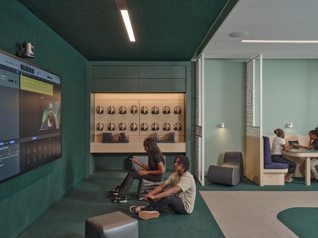 A contemporary collaborative learning or work lounge with deep green acoustic wall and ceiling finishes, an integrated large display, headphone storage, and informal seating. Glazed or open meeting booths are visible to the right, with people working at a shared table. The space uses linear recessed lighting, muted green and grey tones, and built-in joinery.