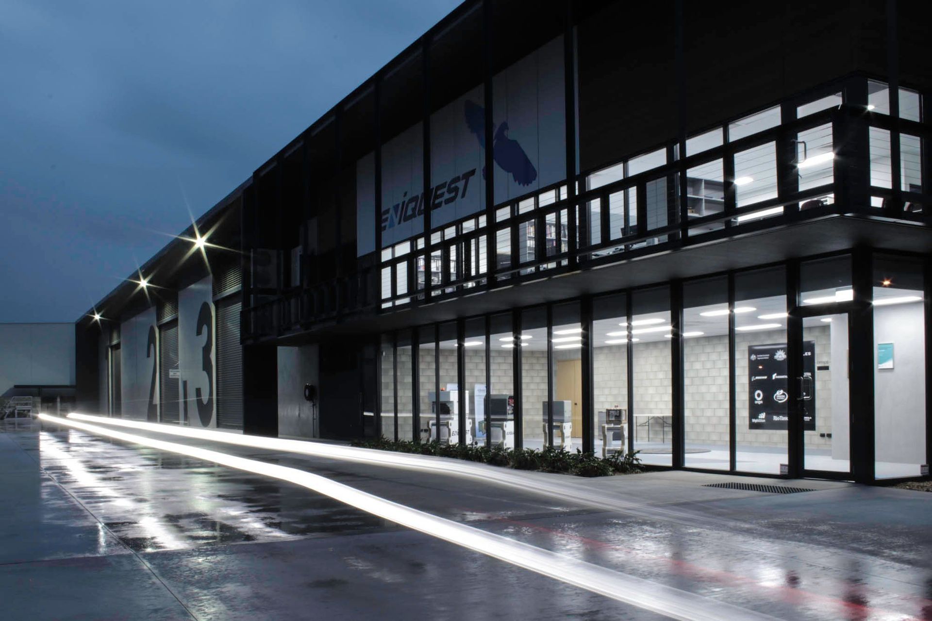 Eniquest Warehouse - Exterior. Glazed office level lit at dusk with light trails.
