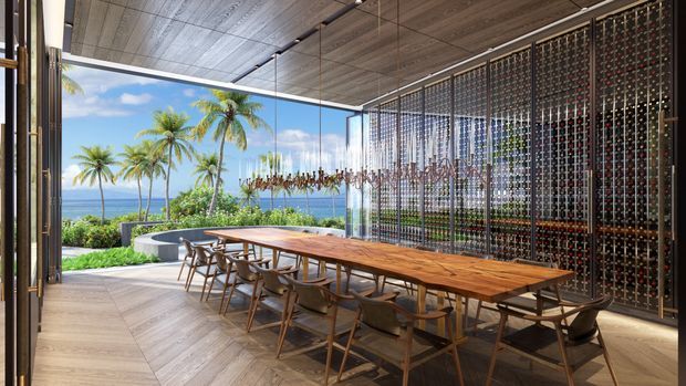 A sophisticated open-air dining pavilion with a long timber dining table and coordinated chairs, opening onto a tropical coastal landscape with palm trees and ocean views. The space features a timber-lined ceiling, timber flooring, slender dark framing, and a dramatic full-height patterned metal screen wall. A curved outdoor seating or poolside element is visible beyond the dining area.