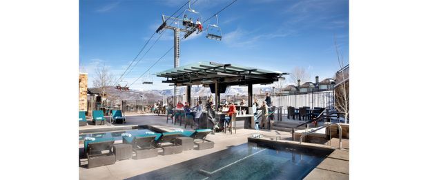 Outdoor resort-style pool and lounge area with a covered bar or pavilion, seating, and a ski lift running overhead. Snowy mountain scenery and a clear blue sky are visible in the background, suggesting a mountain recreation venue.