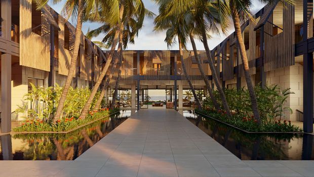 A tropical contemporary resort-style courtyard or covered outdoor passage, framed by multi-storey timber-clad buildings with extensive vertical screening and shaded walkways. A broad paved pedestrian path leads through landscaped planting beds and reflecting water features, with tall coconut palms creating a lush tropical setting. Warm sunlight, timber tones, dark metal framing, and open-air circulation dominate the scene.