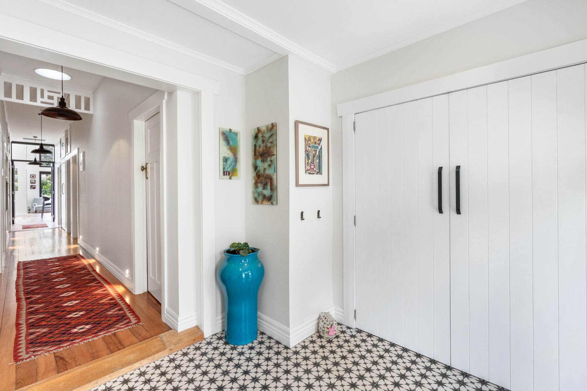 The entry at Devonport Bungalow — encaustic star tiles underfoot, white shiplap storage and a long hallway runner leading the eye through to the garden beyond. Macfie Architecture.