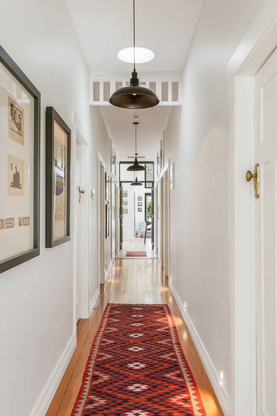 The original hallway at Devonport Bungalow — heritage detailing retained, a kilim runner underfoot and black pendant lights running its full length. Macfie Architecture.