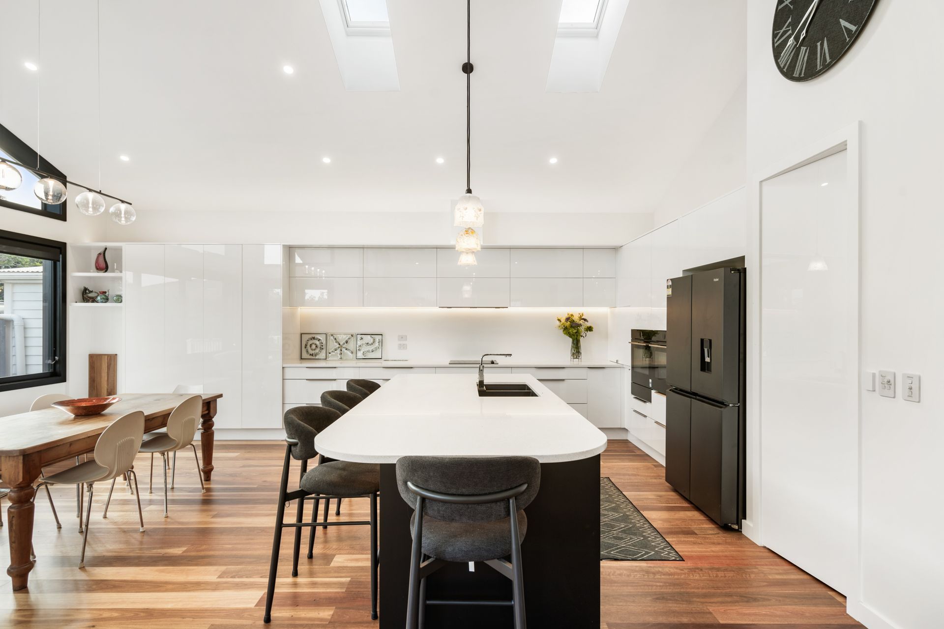 Gloss white cabinetry, a dark island bench and white stone countertop — the kitchen at Devonport Bungalow, where contrast does the talking. Macfie Architecture.