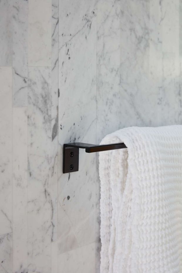 Close-up detail of a wall-mounted dark metal towel rail holding a white textured towel, set against pale veined marble wall tiles in a refined bathroom.