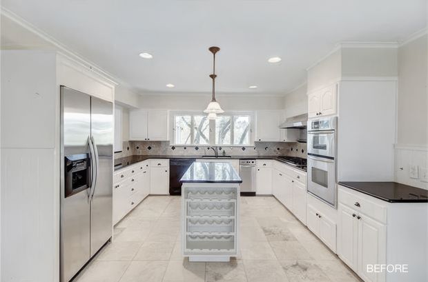 Bright traditional white kitchen shown in a before-renovation view, with extensive white paneled cabinetry, a central rolling island with wine storage, stainless-steel refrigerator and built-in oven, dark patterned benchtops and splashback, tiled flooring, recessed ceiling lights, and a pendant light over the island.