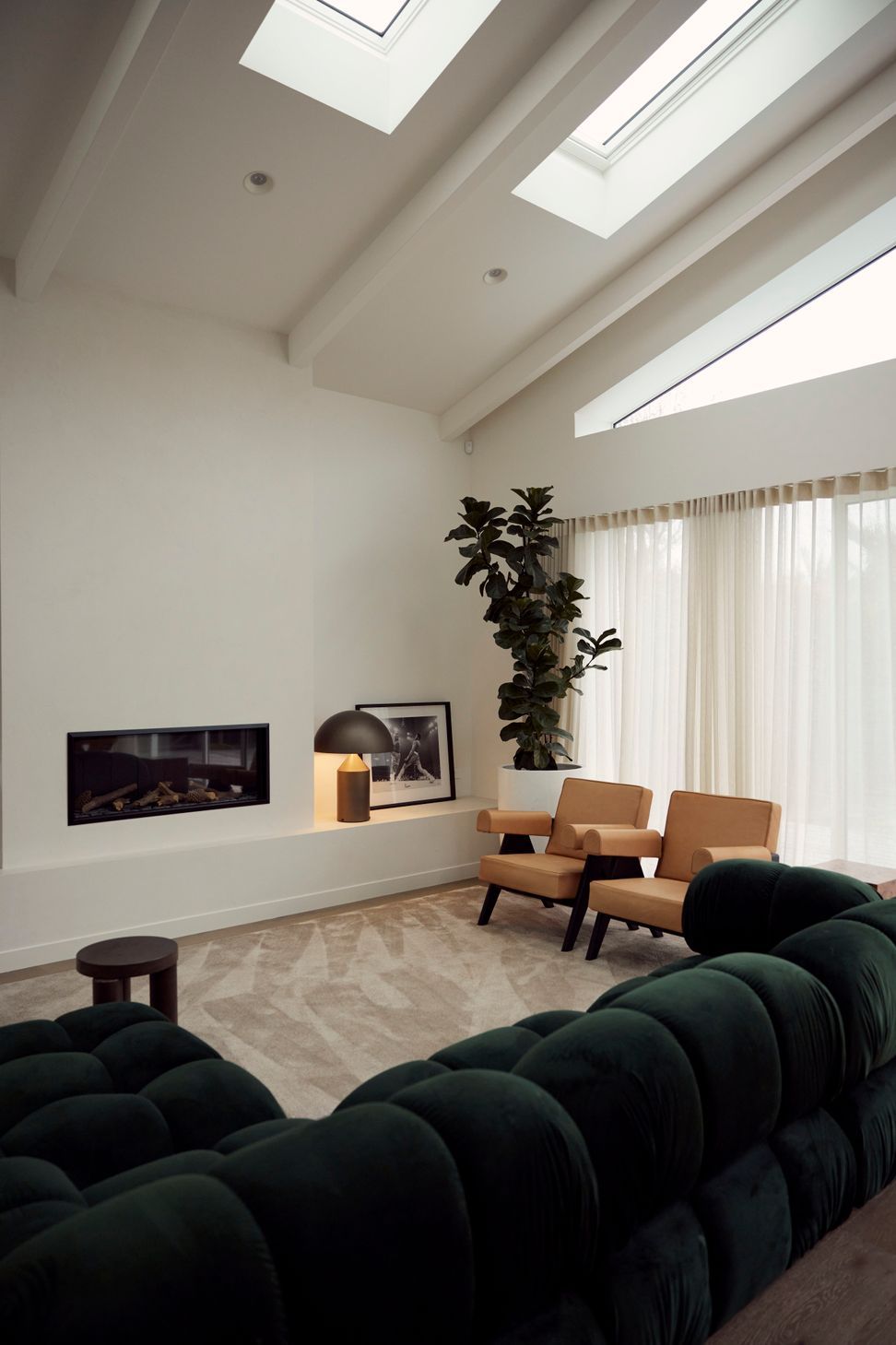 The living room of the rear addition at Point Chevalier Bungalow — skylights flooding the vaulted ceiling with light, a linear fireplace anchoring the space, and Pierre Jeanneret armchairs beside a deep green velvet sofa. In collaboration with Hannah Warren Interiors.