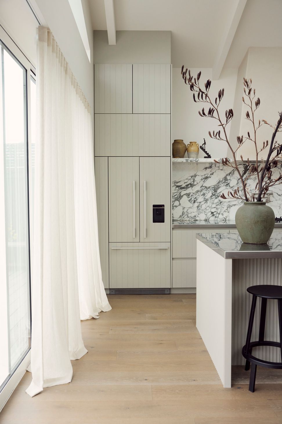 The kitchen at Point Chevalier Bungalow framed by stacking slider doors — Arabescato marble, sage cabinetry and sheer curtains dissolving the line between inside and garden. In collaboration with Hannah Warren Interiors.