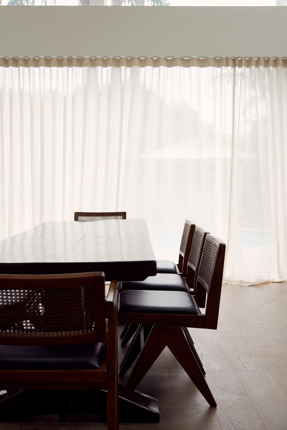 Point Chevalier bungalow dining room with dark timber table, Pierre Jeanneret cane and leather chairs and sheer floor-to-ceiling curtains — Macfie Architecture Auckland