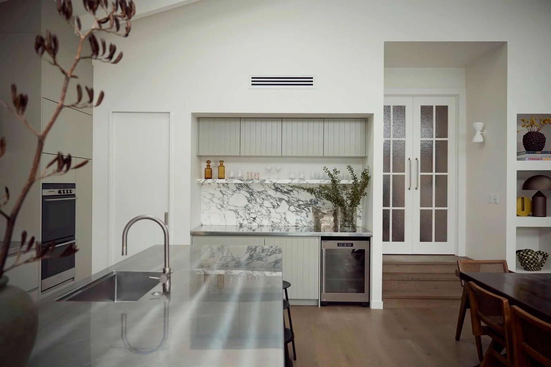 The scullery and bar nook — marble splashback, wine fridge, and sage cabinetry, framed by the textured glass French doors that connect the original bungalow to the new addition. Point Chevalier Bungalow, in collaboration with Hannah Warren Interiors.