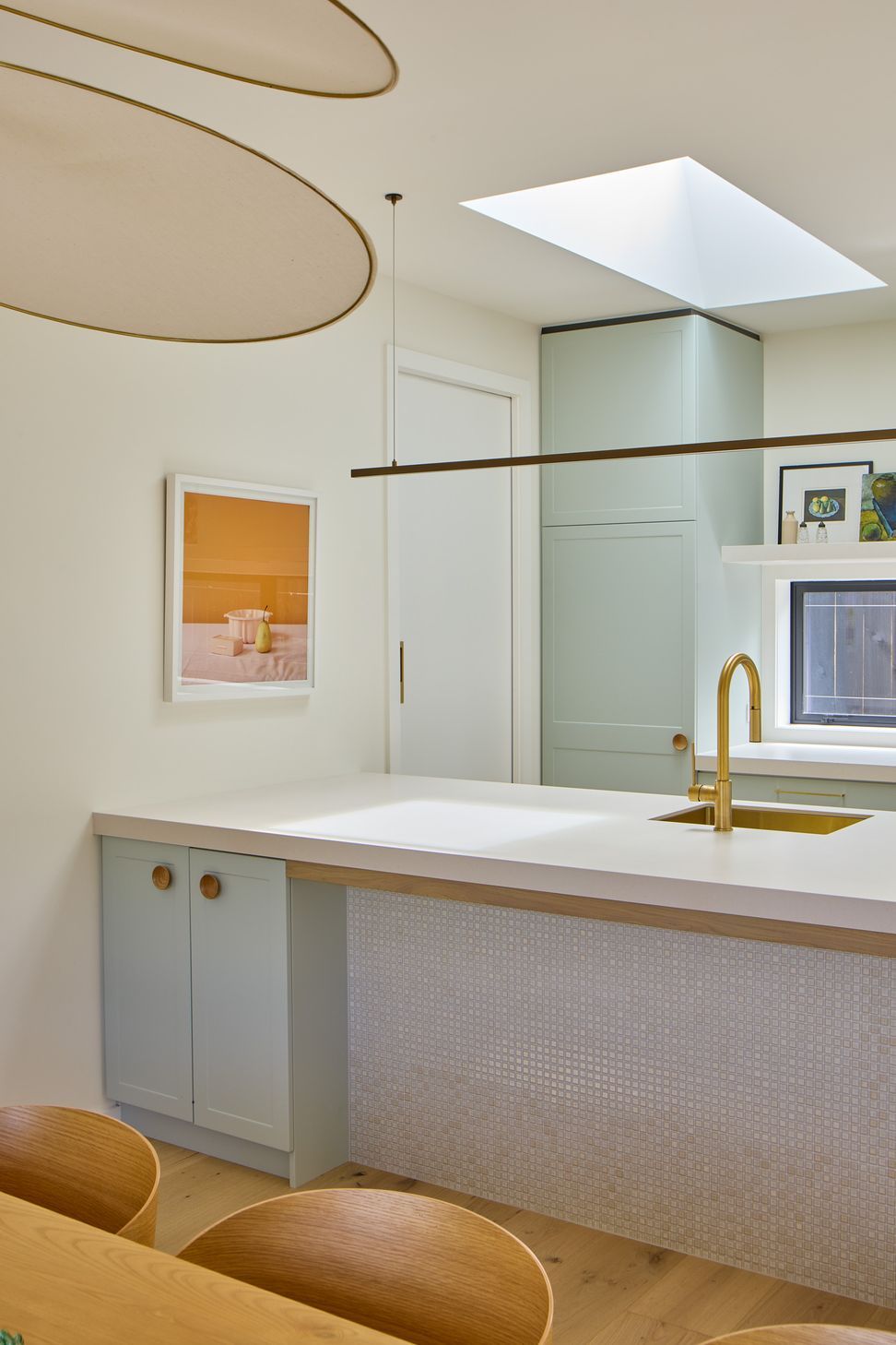 The kitchen sits at the heart of the open-plan living spaces. A generous island with a light grey benchtop, pistachio green cabinetry, rounded oak handles, oak legs and brass fixtures creates a playful yet sophisticated family kitchen.