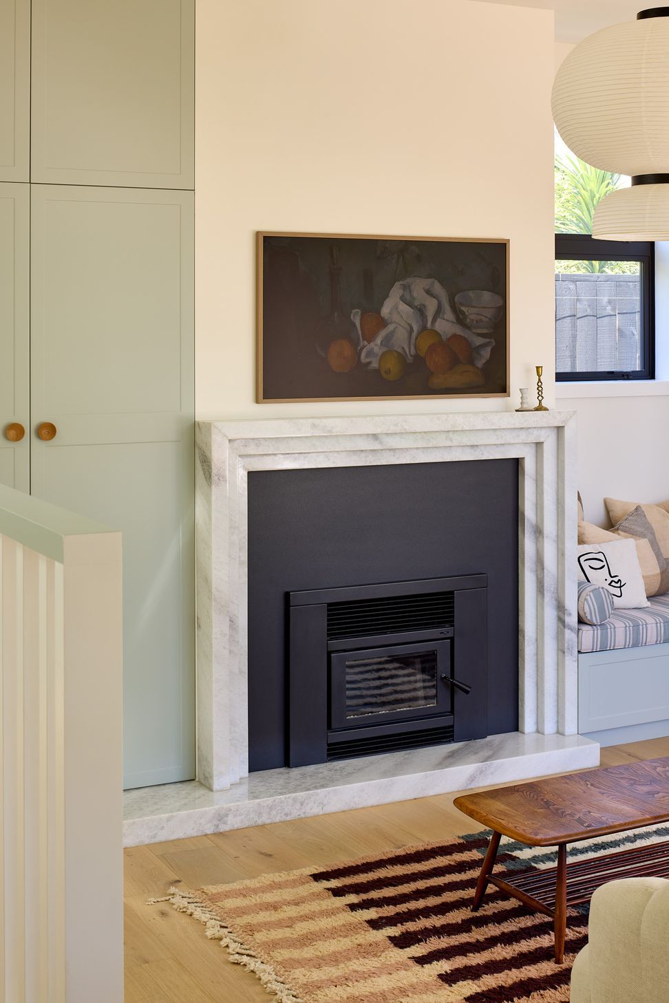 The living room combines bespoke cabinetry with a striking fireplace finished in Super White granite and black steel. A built-in window seat provides a comfortable place to enjoy views of the garden while maintaining a strong connection to the kitchen.