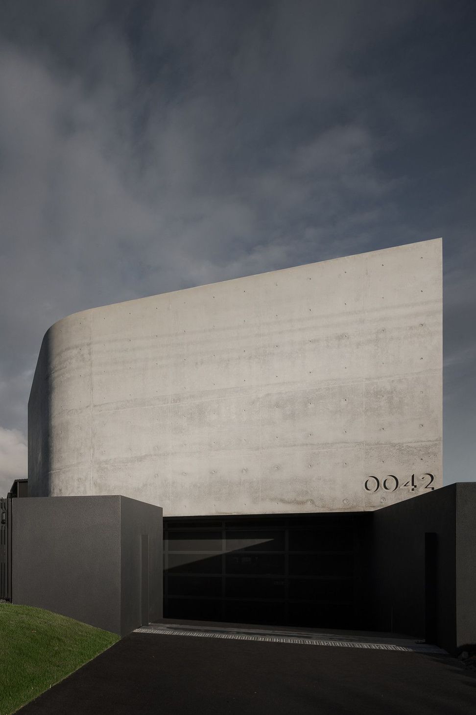 0042 Residence - Exterior. Bold off-form concrete wall guarding the home from the street.