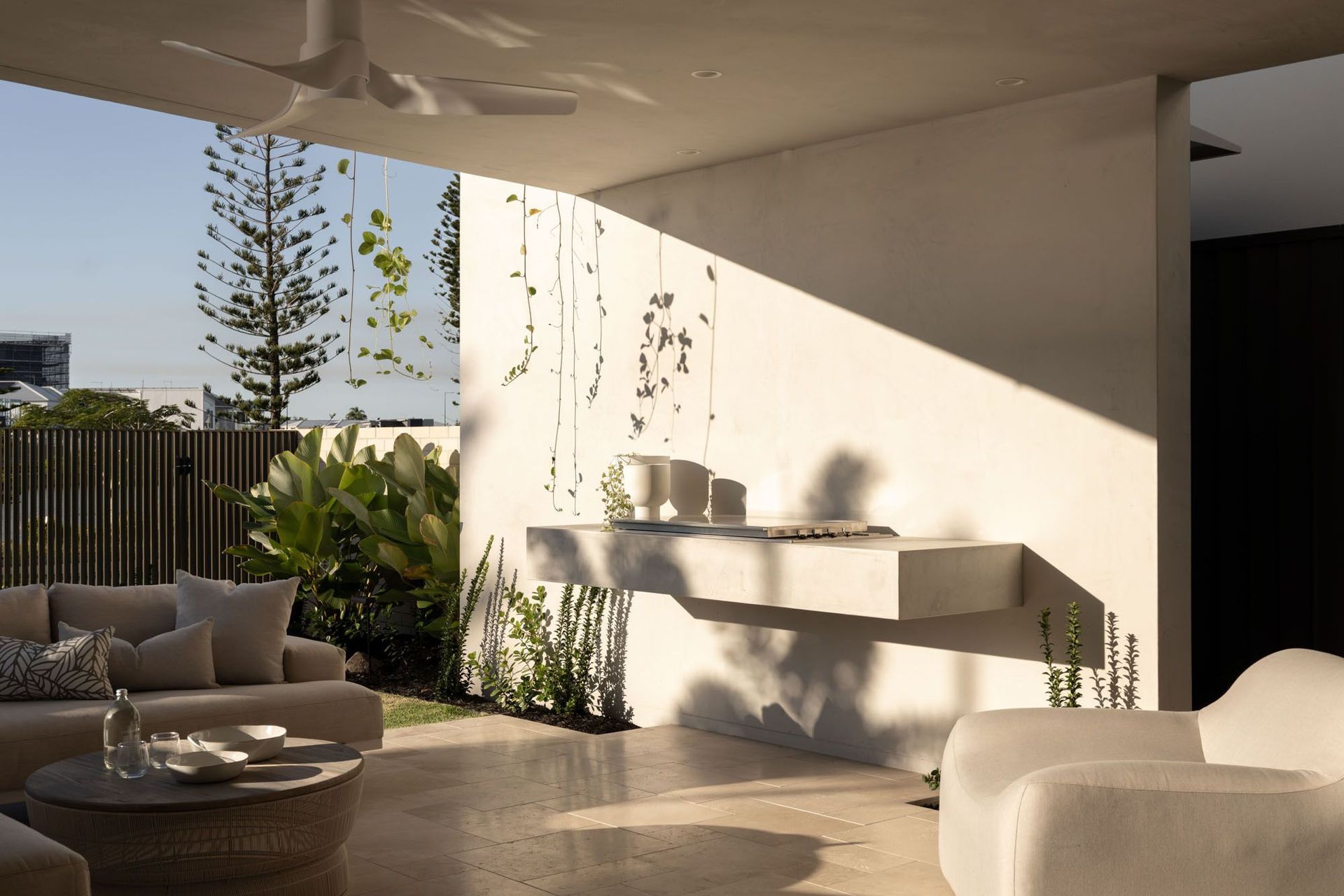 Warrego - Patio. Covered outdoor lounge with a planter wall and palm shadows.