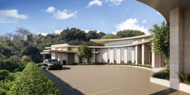 A wide exterior view of a low-slung contemporary residence set into a landscaped site. The building features broad horizontal roof planes, extensive clerestory-style glazing, pale stone or rendered wall surfaces, tall vertical window bays, and a generous paved driveway approached through a covered entry structure. Mature greenery frames the home, with a vehicle parked near the entrance.