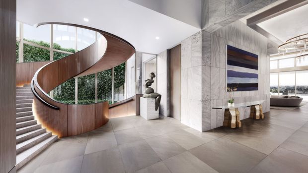 A spacious, high-end contemporary entry foyer dominated by a sculptural curved timber staircase with a flowing open balustrade. Large curved and floor-to-ceiling glazing brings in greenery and daylight, while pale large-format stone or porcelain flooring, light stone wall cladding, and timber detailing create a refined gallery-like interior. A sculptural console and artwork sit beside the circulation space, with a bathtub and additional room visible in the background.
