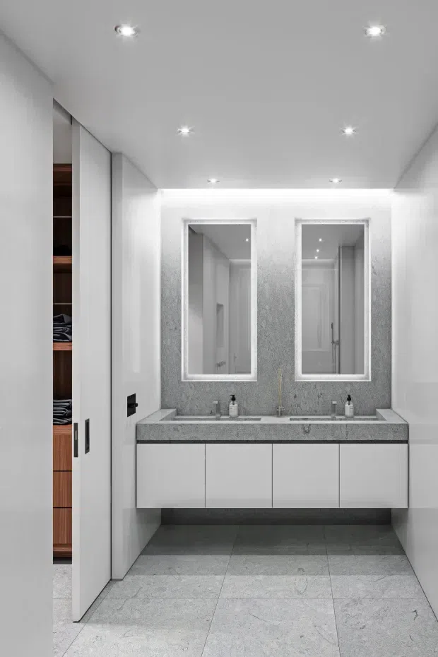 Bright, minimalist double-vanity bathroom with a floating white cabinet, grey stone-look benchtop and matching large-format floor tiles. Two mirrored recessed wall cabinets are set into a textured grey feature wall, with concealed LED downlights and a partially visible walk-in wardrobe or dressing area through the opening at left.